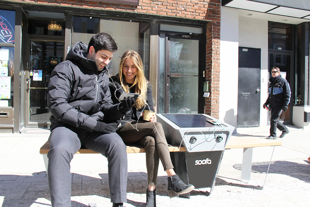 Pedestrians sitting on s Soofa bench